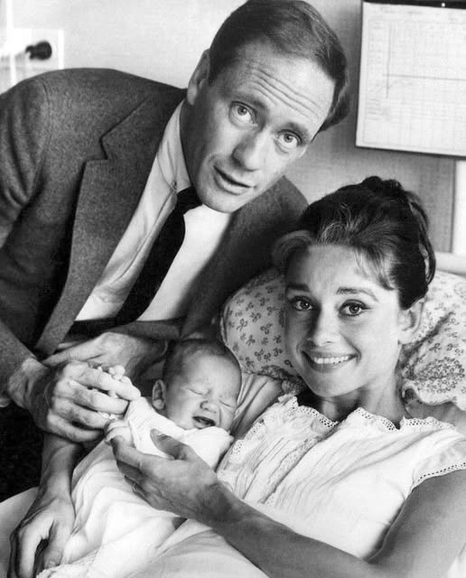 Can you guess who they are?  A timeless family moment captured in 1960 — the radiant couple beams with joy as they welcome their newborn son into the world.