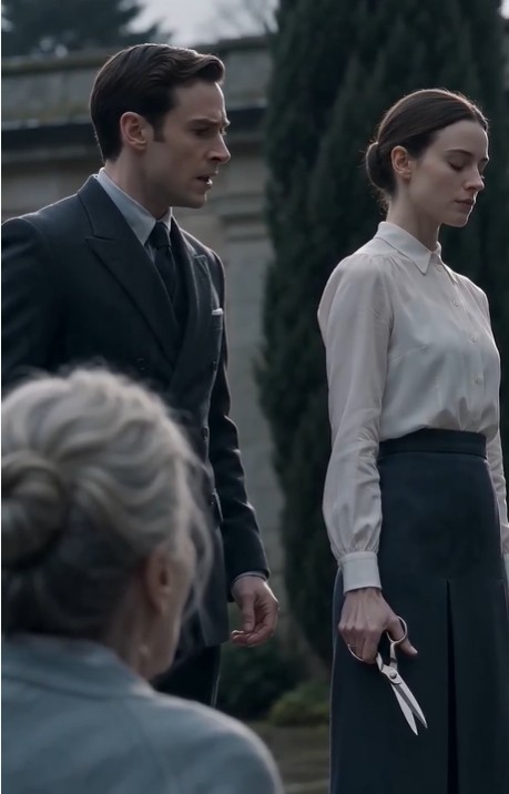 The courtyard feels heavier now.  The man in the dark suit steps closer, his shoes echoing faintly against the stone. His eyes never leave his mother. She is still trembling, barely holding herself upright by the fountain.