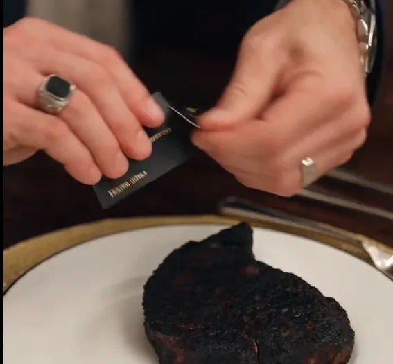 Gloria places a perfect steak in front of Calvin, then drops a completely blackened piece of meat onto Sadie’s plate. Sadie stares at it while Gloria laughs and pushes the plate closer.