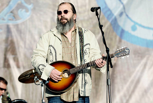 “GUITAR TOWN” MADE STEVE EARLE LOOK LIKE NASHVILLE’S NEXT HARD-COUNTRY STAR. LESS THAN A DECADE LATER, HE WAS OFF THE LABEL, OFF THE CHARTS, AND HEADING TOWARD JAIL. Steve Earle arrived in Nashville at nineteen, already carrying Texas behind him and Townes Van Zandt in his bloodstream. He worked blue-collar jobs, wrote songs, played bass for Guy Clark, and moved through the same rough songwriter world that had shaped Rodney Crowell, Townes, and the post-Kristofferson generation. He was not built like a clean Music Row product. He sounded like a man who had learned country music from truck stops, bad nights, union towns, busted romance, and people who did not get rescued by the last verse. Then came Guitar Town in 1986. The title track hit the country Top 10. Suddenly Earle looked like the bridge Nashville had been waiting for — too tough to be pop, too sharp to be ordinary, too country to ignore. “Goodbye’s All We’ve Got Left” followed into the Top 10, and for a moment, it seemed like the industry had found a new kind of outlaw it could actually sell. But Earle kept moving away from the box. Copperhead Road arrived in 1988 with moonshine blood, Vietnam ghosts, electric guitars, and an Irish-rock charge that country radio could not easily file. It became one of his signature songs, but it also proved the problem: Steve Earle was not going to stay where Nashville put him. Then the road dropped out. Drug abuse and legal trouble pushed him into a recording silence. His label ties broke. The public story grew darker. By the early 1990s, the man who had once looked like country’s dangerous new future seemed like another songwriter being swallowed by the life he wrote about. The comeback did not come dressed like a comeback. In 1995, Earle returned with Train a Comin’, stripped down and acoustic, closer to folk, bluegrass, and old songwriter truth than to the loud machinery that had nearly buried him. A year later came I Feel Alright. Then El Corazón. The voice was still rough, but now it sounded less like rebellion for show and more like a man who had actually come through the fire. That became Steve Earle’s real place in country music. Not the clean outlaw poster. Not the Nashville hitmaker. Not only the man behind “Guitar Town” and “Copperhead Road.” He became a survivor-songwriter — tied to Guy Clark and Townes Van Zandt, covered by major country names, moving between country, rock, folk, bluegrass, protest music, and hard American storytelling without asking permission from any one format. His songs have been recorded by Johnny Cash, Waylon Jennings, Willie Nelson, Levon Helm, The Highwaymen, Travis Tritt, Vince Gill, Patty Loveless, and Emmylou Harris. Steve Earle did not prove he belonged to country by staying pure. He proved it by leaving the road, losing the deal, coming back scarred, and still writing songs that sounded like they had been dragged out of the ditch with the engine running.
