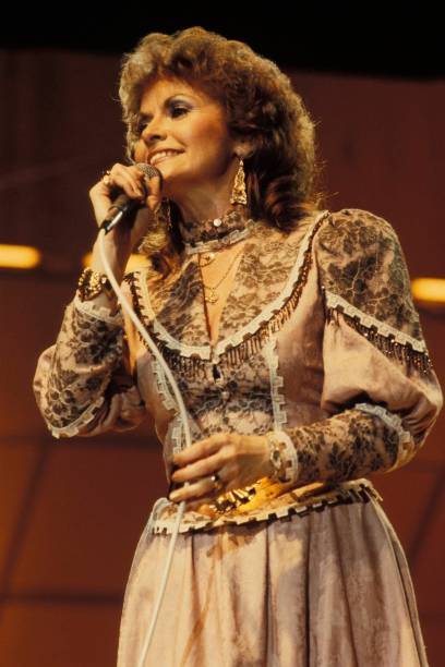 JEANNIE C. RILEY DID NOT EVEN LIKE “HARPER VALLEY P.T.A.” AT FIRST. THEN IT SENT A MUSIC ROW SECRETARY TO NO. 1 ON BOTH THE COUNTRY AND POP CHARTS. Jeannie C. Riley had already discovered what Nashville could do to a young singer’s confidence.  She had left Texas with a husband, a small child, and the belief that a strong voice might be enough to earn a place in country music. But the city was filled with singers carrying the same belief. Jeannie recorded a few unsuccessful singles, sang demonstrations for songwriters, and took office work to help keep her family afloat.  By 1968, she was working as a secretary for songwriter Jerry Chesnut’s publishing company on Music Row.  Then another songwriter needed a woman to sing a demo.  The song was not “Harper Valley P.T.A.” It was Clark Bentley’s “Old Town Drunk,” intended for producer Shelby Singleton at his new Plantation Records label. Singleton listened to the demonstration, but the voice singing it interested him more than the song itself.  He wanted to know who she was.  Singleton had been searching for the right singer for a song written by Tom T. Hall. Hall had built it around Mrs. Johnson, a widowed mother whose teenage daughter returns from school carrying a note from the local parent-teacher association. The committee condemns Mrs. Johnson’s clothes, social life, and parenting.  Mrs. Johnson does not apologize.  She attends the next PTA meeting and publicly exposes the drinking, affairs, and hypocrisy of the respectable people sitting in judgment of her.  Jeannie’s manager urged her to consider the song. Jeannie asked to hear it first.  She was not impressed.  To her, “Harper Valley P.T.A.” sounded too much like an attempt to follow the success of Bobbie Gentry’s “Ode to Billie Joe.” She was also uncertain about Shelby Singleton. Nothing about the offer looked guaranteed. Plantation was a new label, Jeannie was not an established star, and the song was a long, sharply worded story about a woman humiliating an entire small-town committee.  Still, she agreed to record it.  The session took place at Columbia Studio in Nashville. Producer Shelby Singleton kept the arrangement moving underneath Jeannie’s voice, while Jerry Kennedy’s dobro gave the record one of its most recognizable sounds. Jeannie did not sing Mrs. Johnson as a wounded victim. She delivered the words with speed, control, and an edge that made the confrontation feel less like a plea for understanding than a public reckoning.  Plantation released “Harper Valley P.T.A.” in August 1968.  The record exploded.  It climbed to No. 1 on Billboard’s country chart and then reached No. 1 on the Hot 100. Jeannie became the first woman to top both charts with the same recording, an achievement another female artist would not match until Dolly Parton’s “9 to 5” in 1981. The single sold millions of copies and earned Jeannie the Grammy for Best Female Country Vocal Performance, while the Country Music Association named it Single of the Year.  Almost overnight, the Music Row secretary was being dressed, photographed, booked, and promoted as the living version of Mrs. Johnson.  The song’s success gave Jeannie a national audience, but it also created a character large enough to trap the woman singing it. Audiences expected miniskirts, long boots, defiance, and another public confrontation with Harper Valley. Her record company wanted more songs built around similarly outspoken women. The fictional widow became inseparable from the real singer.  There was another complication.  Country music in 1968 still carried strict expectations for women. Jeannie was marketed through the same appearance that made Mrs. Johnson controversial inside the song. The short skirts helped sell the image, but they also drew criticism from parts of the country audience that embraced traditional values while buying a record about exposing other people’s double standards.  The contradiction was almost too perfect.  A song attacking small-town hypocrisy had turned its singer into an object of judgment.  Jeannie continued placing records on the country chart, including “The Girl Most Likely,” “There Never Was a Time,” and “Country Girl.” She hosted a network television special and remained a recognizable star into the early 1970s. But nothing could realistically follow a debut that had reached the top of two musical worlds at once. “Harper Valley P.T.A.” remained the standard against which every later release was measured.  The woman in Tom T. Hall’s song walked into a meeting and named every hypocrite in the room.  The woman who recorded it walked out of a secretary’s office and into country music history.  But from then on, wherever Jeannie C. Riley went, Mrs. Johnson was already waiting for her.