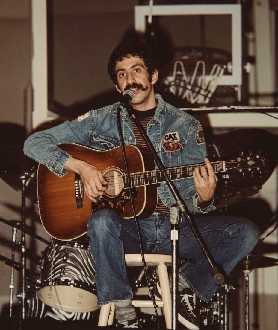 Jim Croce seated with an acoustic guitar and microphone