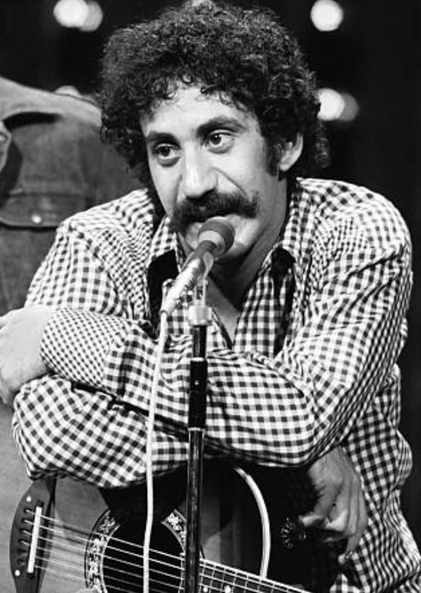 Jim Croce speaking at a microphone with guitar